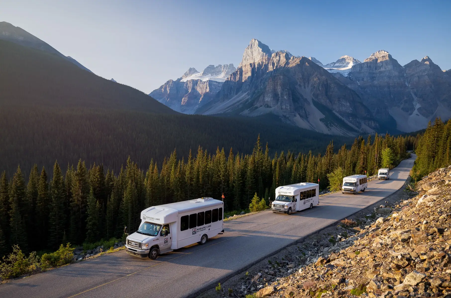 A few shuttle buses on a mountain road surrounded by stunning peaks. 